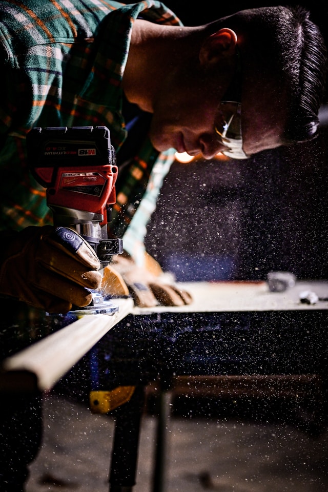Craftsman using a power tool to shape wood, with sawdust flying in the air. The focused work highlights craftsmanship in a workshop setting.