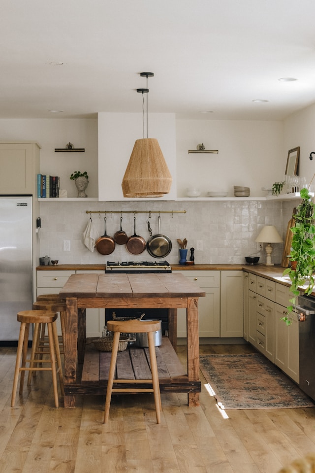 Bright, modern kitchen featuring a wooden island, hanging pendant light, and sleek cabinetry. Cookware is neatly arranged on a wall rack.