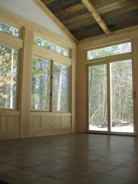 Bright, airy room with large windows and wood accents, overlooking a forested area. Suitable for relaxation or nature observation.