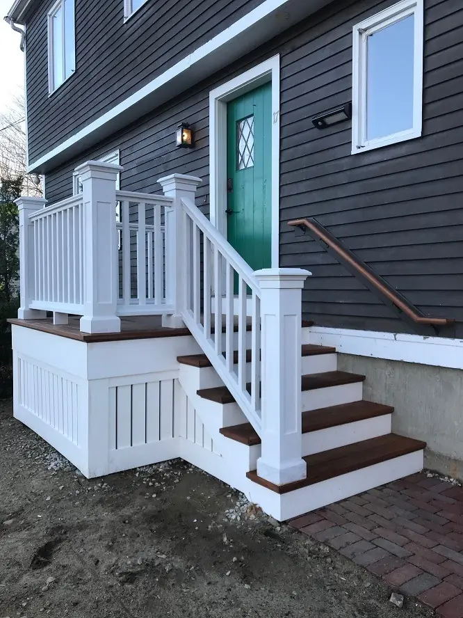 Exterior entrance featuring a green door and white railings, flanked by stairs and a decorative landing, enhancing the home’s appeal.