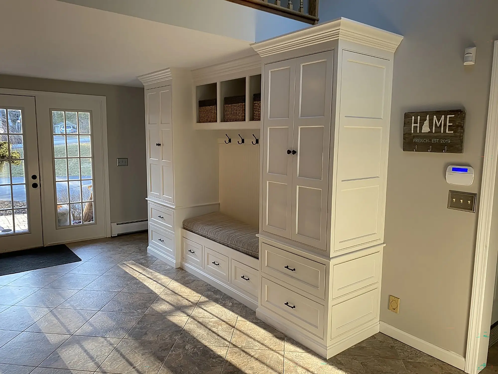 Bright entryway features a white built-in storage unit with a bench, hooks for hanging items, and decorative baskets, enhancing organization and style.