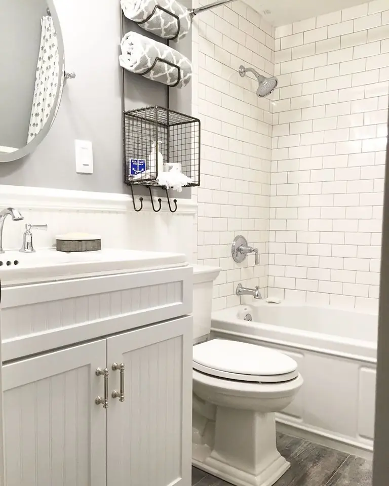 Modern bathroom featuring a white vanity, round mirror, gray patterned towels, and subway tile. Organized storage enhances functionality and style.