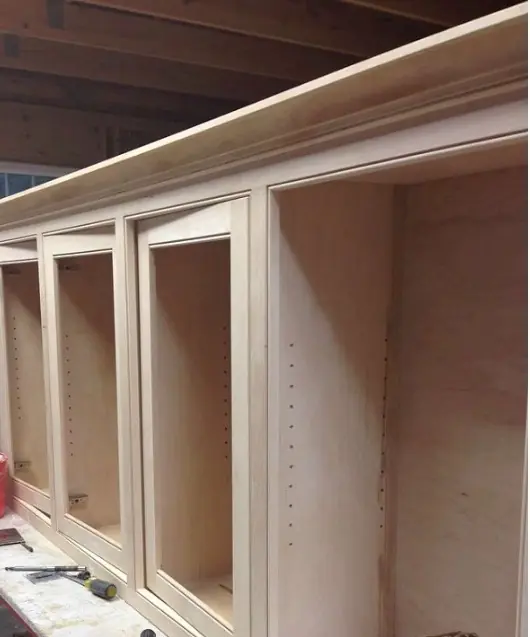 Wooden cabinet framework with four open compartments, showcasing unfinished construction details and tools, illustrating custom cabinetry work.
