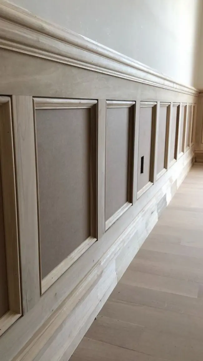 Stylish wooden wainscoting featuring clean lines and a decorative top rail, set against a pale wall in a bright interior space.