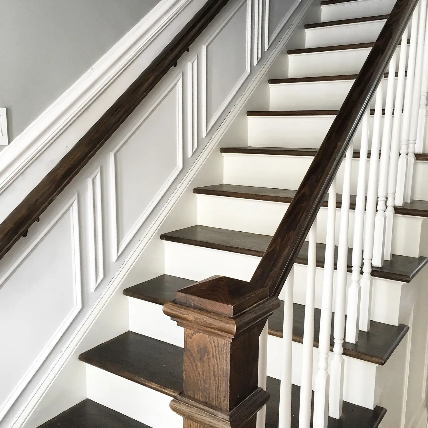 Elegant staircase with dark wooden steps and white risers, featuring detailed wainscoting and a polished wooden handrail, showcasing modern home design.