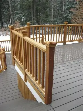 Wooden deck railing curves around a snow-dusted surface, surrounded by trees. This image illustrates outdoor home design and winter aesthetics.