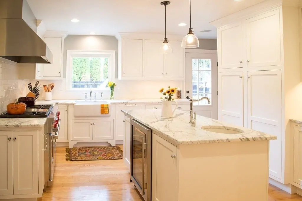 Bright, modern kitchen featuring white cabinetry, marble countertops, and a farmhouse sink. Sunflowers in a vase add a cheerful touch.