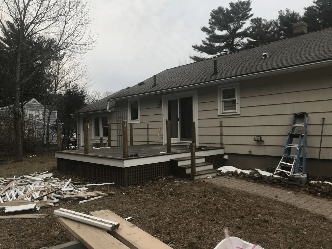Under-construction back deck of a house, featuring wooden posts and debris scattered on the lawn, highlighting ongoing home improvements.